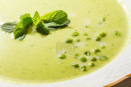 Bowl of green pea soup with mint leaves.