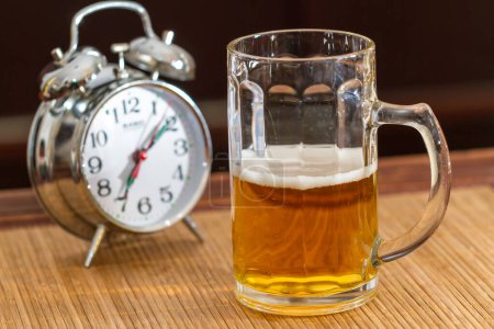 Téléchargez les photos : Tasse en verre à moitié pleine de bière et un vieux réveil en argent - en image libre de droit