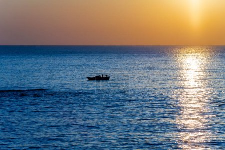 Téléchargez les photos : Vue panoramique du coucher de soleil coloré de l'océan avec petit bateau de pêche silhouette au premier plan. - en image libre de droit