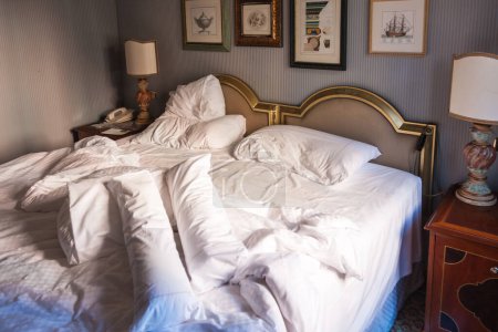 Foto de Cama deshecha arrugada en un elegante dormitorio interior con cabeceros dobles, papel pintado y mesitas de noche con lámparas - Imagen libre de derechos