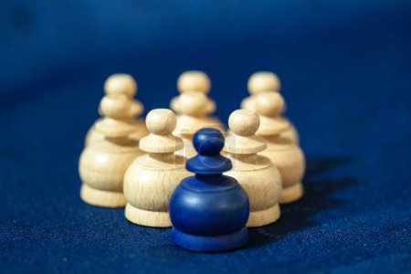 Photo for A close up of white chess pieces in a group, with a single blue pawn at the front on a blue background. - Royalty Free Image
