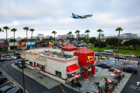 Téléchargez les photos : Los Angeles, Californie, États-Unis - 26 mai 2022 : Avion Alaska Airlines survolant un restaurant vintage In-N-Out Burger lors de l'atterrissage au LAX de l'aéroport international de Los Angeles. - en image libre de droit
