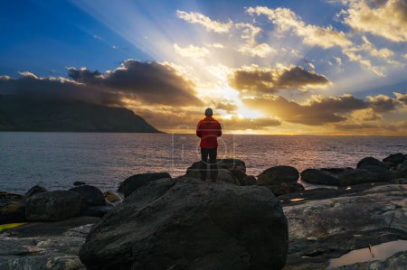 Téléchargez les photos : Randonneur debout sur la plage Tungeneset au coucher du soleil avec des montagnes sous de lourds nuages en arrière-plan, île Senja, Norvège du Nord - en image libre de droit