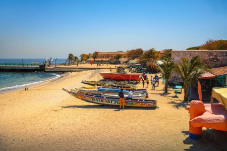 Téléchargez les photos : Goree, Sénégal - 01 mars 2023 : Bateaux de pêche colorés sur une plage de sable fin à Goree Island avec océan et jetée en arrière-plan. - en image libre de droit