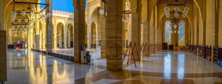 Foto de Manama, Bahréin - 24 de diciembre de 2023: Interior iluminado por el sol de la Gran Mezquita Al Fateh con arcos y faroles colgantes. Es la mezquita más grande de Bahréin, con una exquisita arquitectura islámica. - Imagen libre de derechos