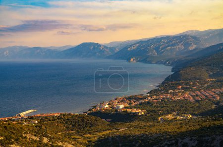 Coastal village of Cala Gonone in Sardinia during sunset, photographed from above with surrounding mountains and Tyrrhenian Sea.