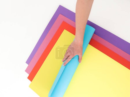 Photo for A hand holds a blue paper against a background of colorful paper. Place for text and logo. The concept of training, decor, needlework. High quality photo - Royalty Free Image