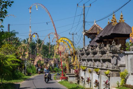 Foto de BALI, INDONESIA - 16 DE ABRIL DE 2017: Calles de Bali. Los polacos Penjor pueden ser vistos como parte de la celebración anual de Galungan. Una persona en una bicicleta se puede ver. - Imagen libre de derechos