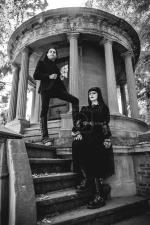Téléchargez les photos : Couple gothique foncé dans un grand ancien mausolée abandonné de style néoclassique avec colonnes et escaliers dans la forêt - en image libre de droit