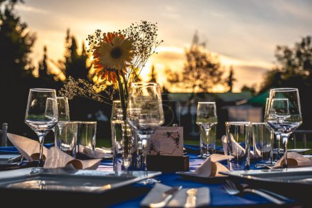 Téléchargez les photos : Bouquet de tournesol et de petites fleurs blanches dans une table de mariage avec des lunettes et un décor de table élégant au coucher du soleil - en image libre de droit