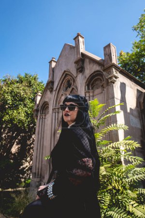 Téléchargez les photos : Stylish dark gothic girl in large ancient abandoned mausoleum with neoclassical style with blue sky in a sunny day - en image libre de droit