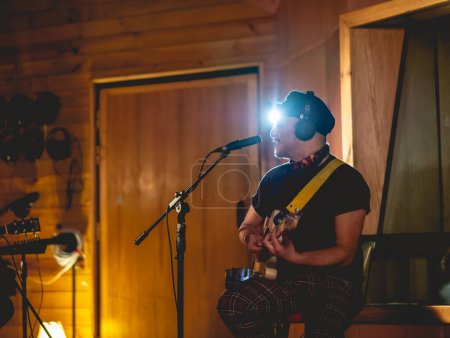 Téléchargez les photos : Young rocker musician with biker hat playing a cream electric guitar and singing in a music studio - en image libre de droit