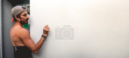 Téléchargez les photos : Fit jeune travailleur latino mettre une vis dans un trou avec sa main dans une porte en acier d'une zone électronique (panoramique avec grand espace de copie) - en image libre de droit