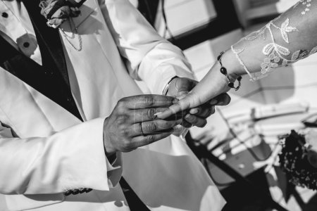 Téléchargez les photos : Le moment d'amour parfait : détail des mains du marié mettant la bague sur le doigt de la mariée (en noir et blanc) - en image libre de droit