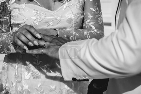 Téléchargez les photos : Le moment d'amour parfait : détail des mains de la mariée mettant une bague sur le doigt du marié (en noir et blanc) - en image libre de droit