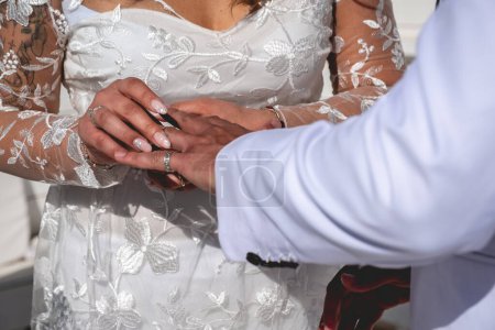 Téléchargez les photos : Le moment d'amour parfait : détail des mains de la mariée mettant une bague sur le doigt du marié - en image libre de droit