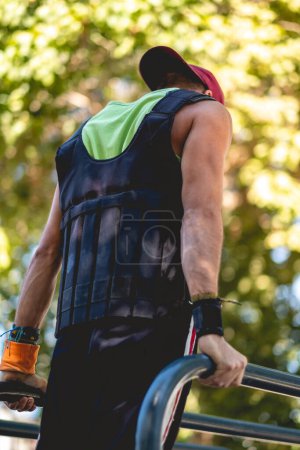 Photo for Sunny street workout: latin male athlete with training vest exercising on parallel bars in urban park - Royalty Free Image