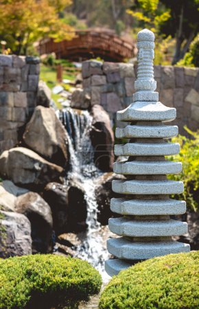 Téléchargez les photos : Oasis zen paisible : jardin japonais orné d'une douce cascade, étang serein, lampe en pierre et verdure luxuriante par une journée ensoleillée - en image libre de droit