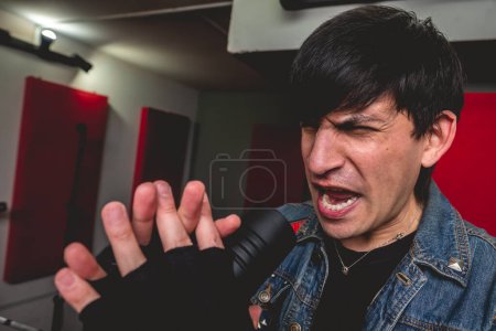 Téléchargez les photos : Jeune chanteur rock passionné et intense déchaînant de l'énergie brute lors d'un concert de métal intense dans une salle de répétition - en image libre de droit