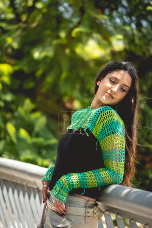 Téléchargez les photos : Nature et latina beauté : Jeune modèle brune avec un pull tricoté vert entre nature verte et rayons du soleil dans le parc - en image libre de droit