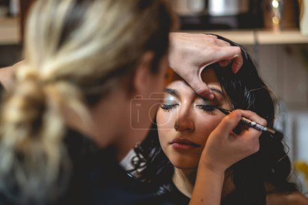 Foto de La belleza de la preparación: un maquillador preparando a una hermosa y joven modelo morena para una sesión de fotos - Imagen libre de derechos