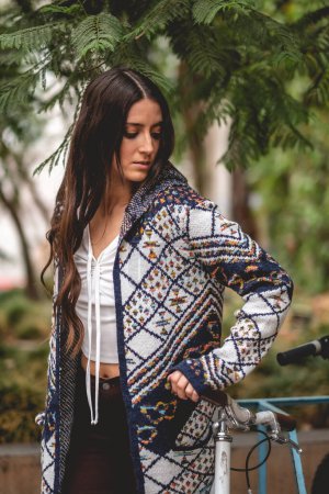 Téléchargez les photos : Mode latino et beauté : Jeune modèle brune avec un pull tricoté coloré traditionnel dans un parc avec des arbres et des vélos - en image libre de droit