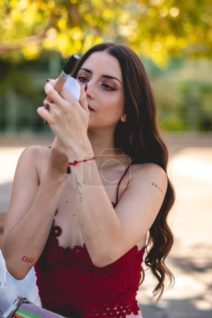 Ritual de belleza natural: joven morena latina realza sus rasgos con maquillaje en el entorno sereno del parque