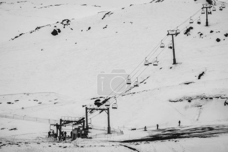 Téléchargez les photos : De joyeux moments d'hiver : remontées mécaniques et petites silhouettes ludiques contre la neige claire dans une belle vue sur la colline (en noir et blanc) - en image libre de droit
