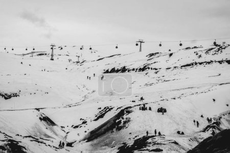 Téléchargez les photos : De joyeux moments d'hiver : remontées mécaniques et petites silhouettes ludiques contre la neige claire dans une belle vue sur la colline (en noir et blanc) - en image libre de droit