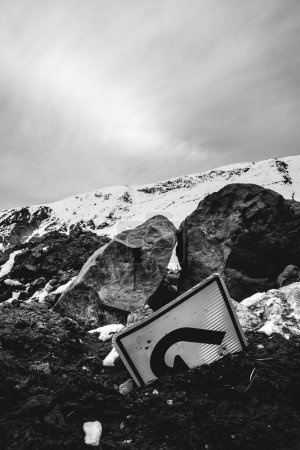 A turn in the cold: a solitary "u turn" sign lost in the snow and rocks of a snowed mountain peak (in black and white)