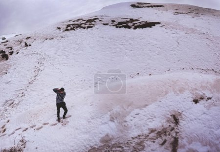 Capturez les hauteurs : un jeune photographe se promène dans un paysage de montagne enneigé pour une prise de vue panoramique parfaite