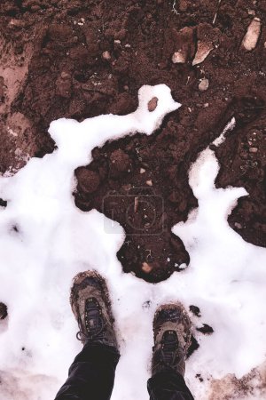 Crossing climates: mountain trekker's feet poised on the boundary between snow and mud, a symbol of global warming's impact