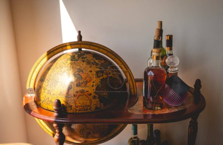 Oldtimer-Reisen: Alte Erdkugel in einer klassischen hölzernen Bar-Station mit antiken Alkoholflaschen geschmückt