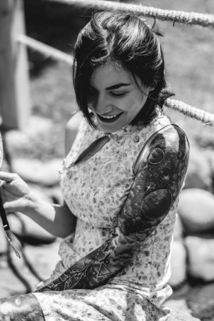 Multi cultural fusion: beautiful latin woman in an asian dress, relaxing by a water stream in a japanese garden with a paper fan (in black and white)