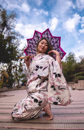 Téléchargez les photos : Tradition et beauté : femme aux cheveux blonds japonais en kimono de soie blanche avec motif de fleurs et parapluie rose dentelle au parc japonais serein - en image libre de droit