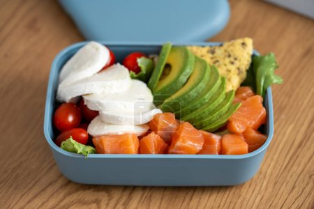 Caja de lanza con comida saludable. Salmón, aguacate, queso, tomate. Comida adecuada contigo en un recipiente. Alimentos útiles para el trabajo.