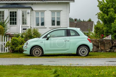 Foto de Lindesnes, Noruega - 07 de agosto de 2022: Coche Fiat 500 verde menta de casas tradicionales de madera blanca. - Imagen libre de derechos