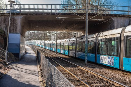 Gothenburg, Sweden - March 31 2020: Extra long blue and white commuter train passing under a bridge.