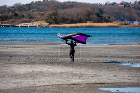 Photo for Gothenburg, Sweden - March 13 2022: Person walking on a beach getting ready to wing foil. - Royalty Free Image