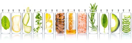 Foto de Homemade skin care with natural ingredients avocado ,aloe vera ,cucumber ,himalayan salt  ,honeycomb ,almonds, ginger slice and rosemary  in glass bottles isolate on white background. - Imagen libre de derechos