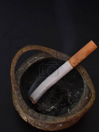 Photo for Cigarettes extinguished in a metal ashtray on a black background - Royalty Free Image