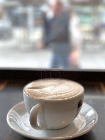 une tasse de cappuccino près de la fenêtre et un passant passe