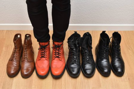 Téléchargez les photos : Un homme en pantalon noir se tient dans des chaussures orange sur le sol près de chaussures noires et marron - en image libre de droit