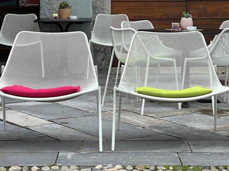 metallweiße Stühle mit farbigen Kissen stehen draußen