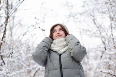 Téléchargez les photos : Portrait de jeune femme regardant vers le haut sur la nature hivernale, jolie belle fille parmi les arbres couverts de neige marchant dans la forêt blanche et profitant - en image libre de droit