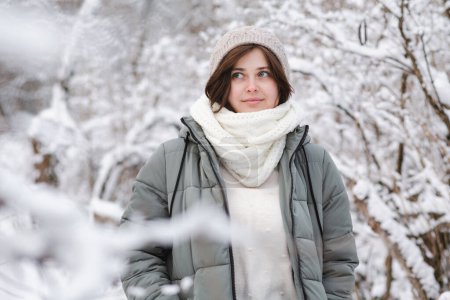 Téléchargez les photos : Jolie jeune femme en vêtements d'hiver parmi les branches d'arbre recouvert de neige, fille marchant dans la forêt enneigée jouissant d'une belle nature - en image libre de droit