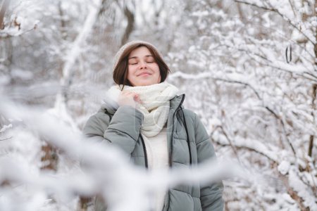 Téléchargez les photos : Jolie jeune femme en vêtements d'hiver parmi les branches d'arbre recouvert de neige, fille marchant dans la forêt enneigée jouissant d'une belle nature - en image libre de droit