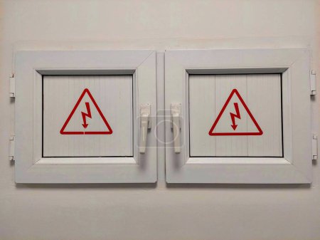 Foto de Dos pequeñas puertas protegen la red eléctrica. En la puerta hay un símbolo del rayo en un triángulo. La señal de advertencia es tensión eléctrica. Peligro de choque eléctrico de alto voltaje signo aislado triángulo. - Imagen libre de derechos
