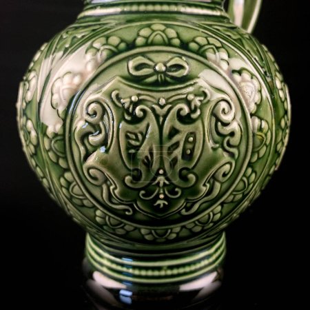 Photo pour Ancienne cruche en céramique verte avec des motifs nationaux. cruche vintage avec un ornement sur fond noir isolé - image libre de droit