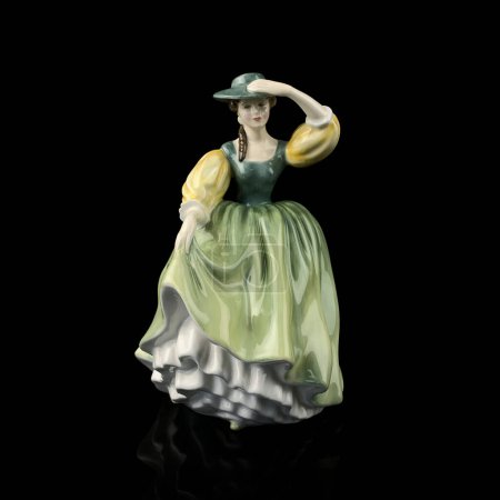Téléchargez les photos : Porcelain figurine of a woman in a green dress on a black background. vintage figurine of a woman in a retro dress. the dress moves with the wind - en image libre de droit
